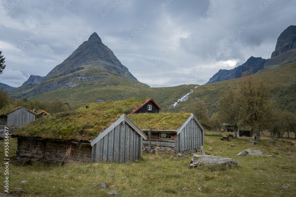 Old wooden huts with green grass on roof in front of landmark mountain in Norway Old wooden huts with green grass on roof in front of landmark mountain in Norway