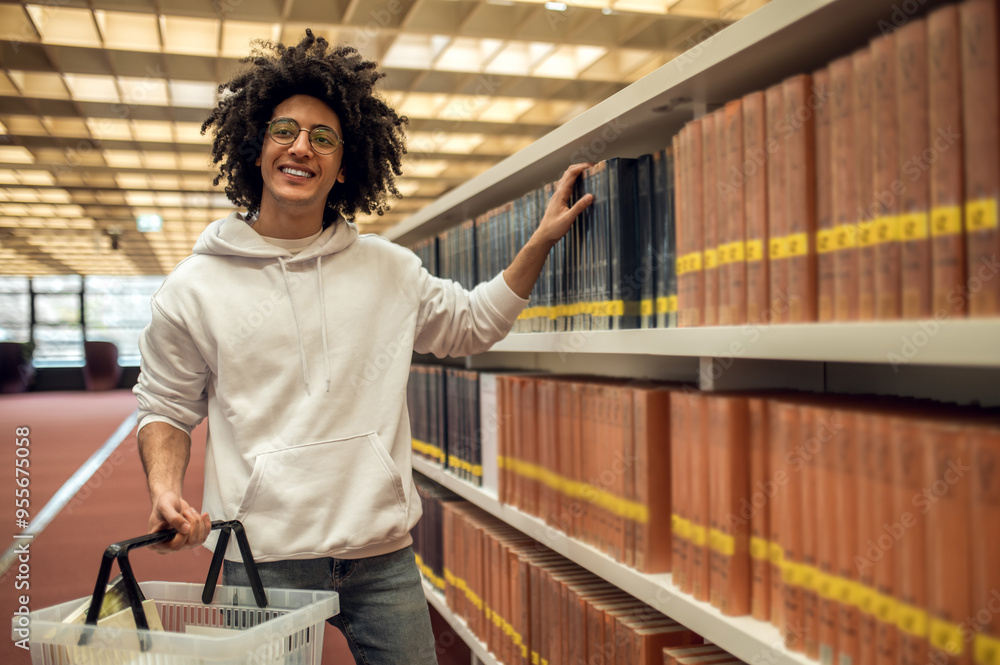 Young man in library taking book from shelf preparing for exams Young man in library taking book from shelf preparing for exams