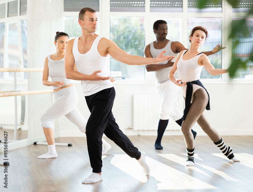 Obraz premium Motivated young adult man participating in group ballet class, practicing graceful dance movements in bright choreography studio with natural lighting..