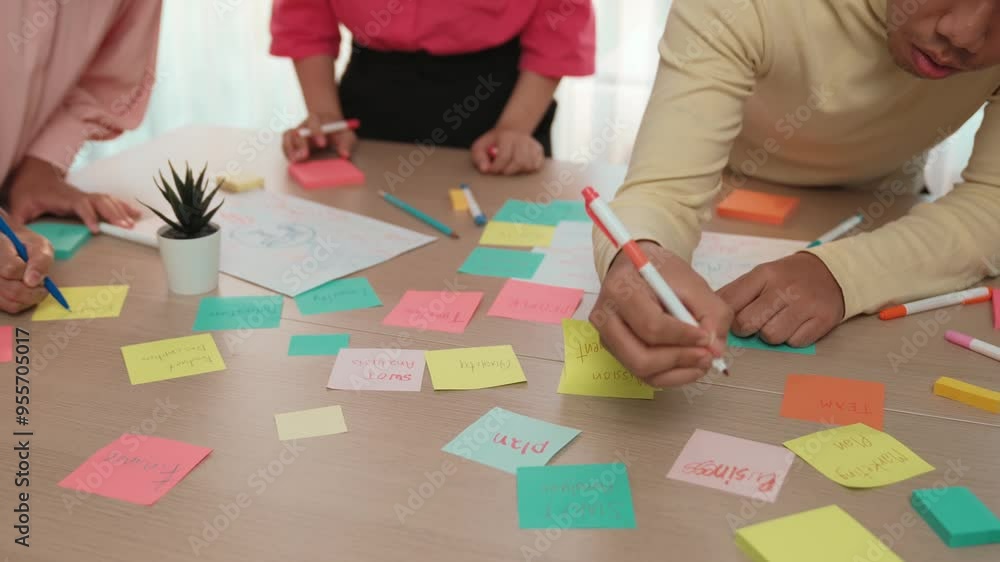 Slow motion hand closeup of startup employee team brainstorming strategic marketing plan and making mind map with colorful sticky notes placed on office table at meeting room. Variegated Slow motion hand closeup of startup employee team brainstorming strategic marketing plan and making mind map with colorful sticky notes placed on office table at meeting room. Variegated