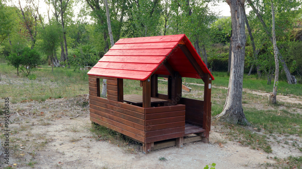 A charming wooden playhouse with a bright red roof stands alone in a grassy area, surrounded by trees under a clear blue sky, inviting imaginative play. A charming wooden playhouse with a bright red roof stands alone in a grassy area, surrounded by trees under a clear blue sky, inviting imaginative play.