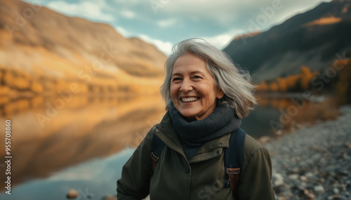 Portrait of an elderly woman with a bright smile on the shore of a lake in the mountains. Autumn landscape.