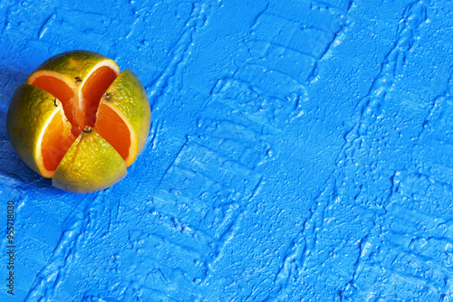 An orange with peel cut into quarters on a blue background with diagonal blue textured stripes