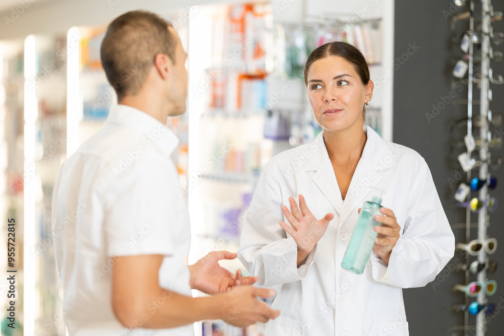 Obraz premium Positive woman apothecary speaking to male customer holding hygienic preparation in pharmacy store