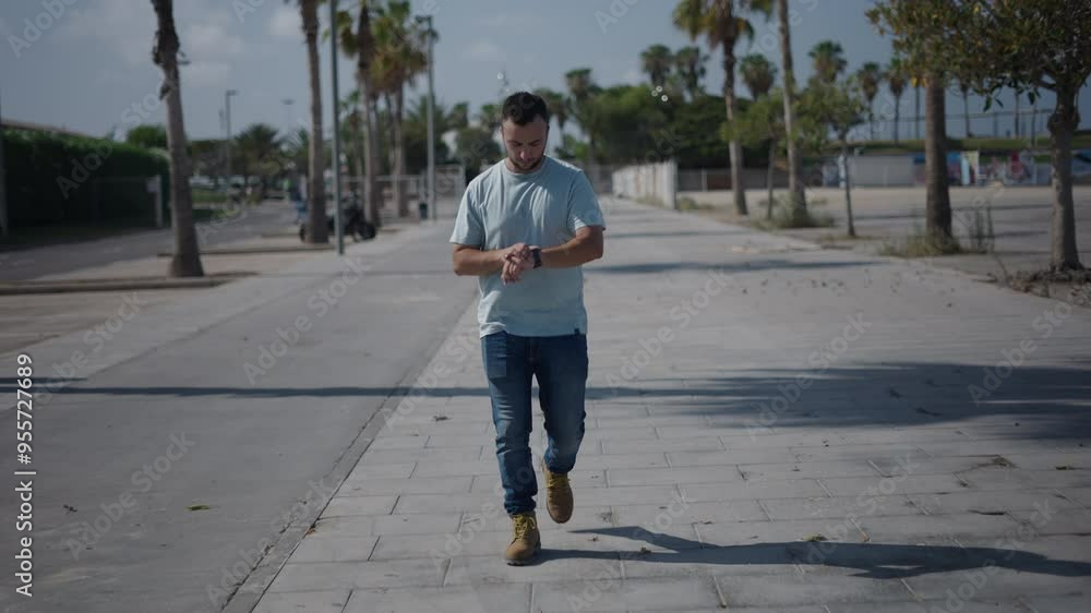 Young Caucasian boy walking in profile to the camera along the cement walkway between palm trees sends a voice note with his smartwatch Young Caucasian boy walking in profile to the camera along the cement walkway between palm trees sends a voice note with his smartwatch