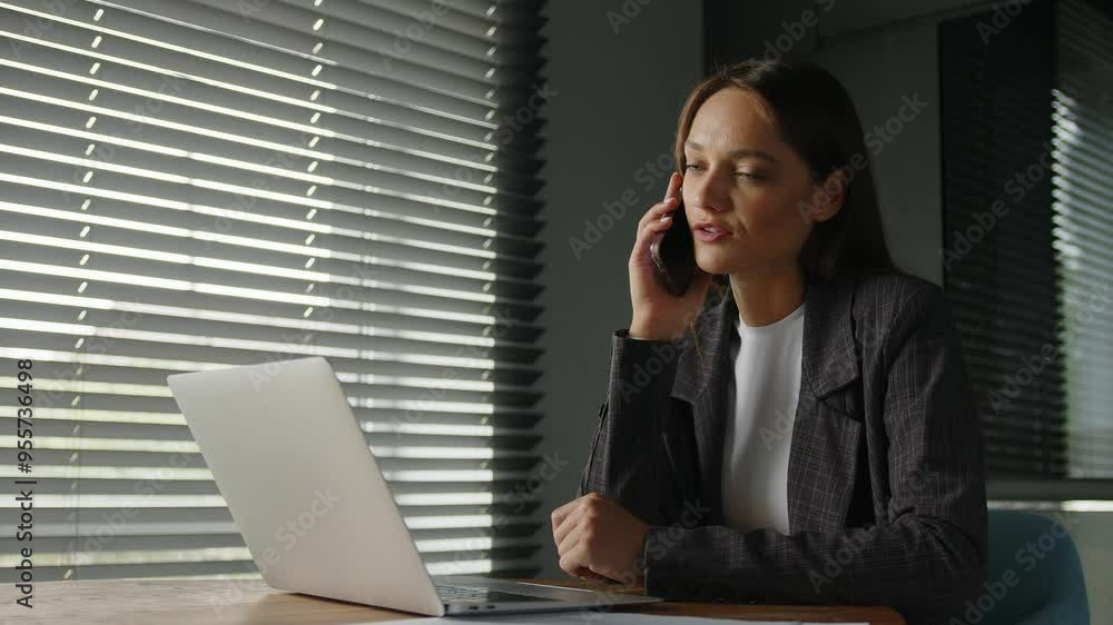 Young busy woman working on project documents talking on the phone. Female manager making business call on phone working alone in office.