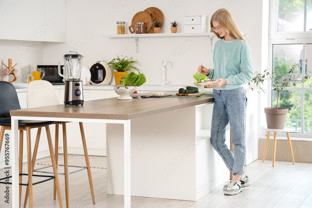 Young woman eating salad with feta cheese in kitchen Young woman eating salad with feta cheese in kitchen
