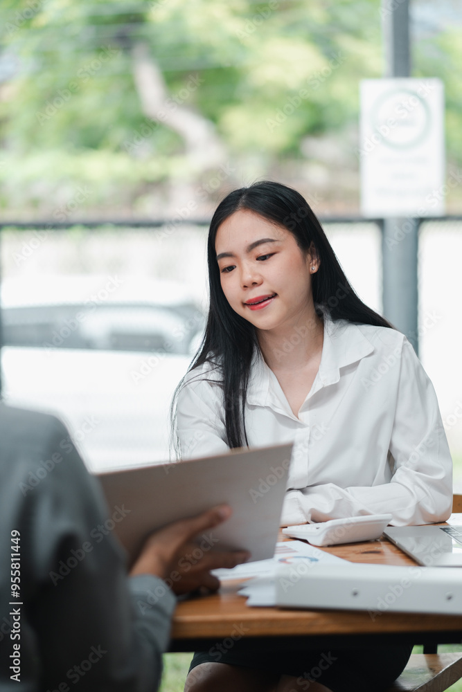 A young woman in a white shirt attentively listens during a business meeting in a modern office environment. A young woman in a white shirt attentively listens during a business meeting in a modern office environment.