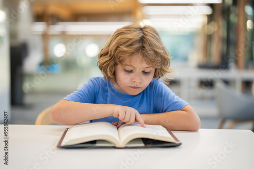 Kid reading book. Child reading book in a public library. Education and school concept. Little student studying and reading book at school library.