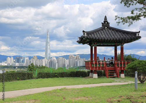 Gangnam-gu, Seoul, South Korea - September 4, 2021: Summer view of tourists on a pavilion at Cheongdam Baesuji Parkag ainst Lotte World Tower and highrise apartments near Han River photo