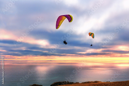 San Diego, California, USA - June 6, 2021: Sunset view of two paragliding riders flying over Black's Beach against sea horizon in summer