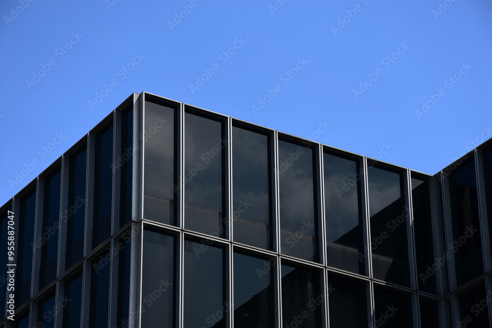 This image captures a modern glass building with a reflective facade, mirroring the vibrant blue sky and shadow. The interplay of light, silhouette, and reflection.