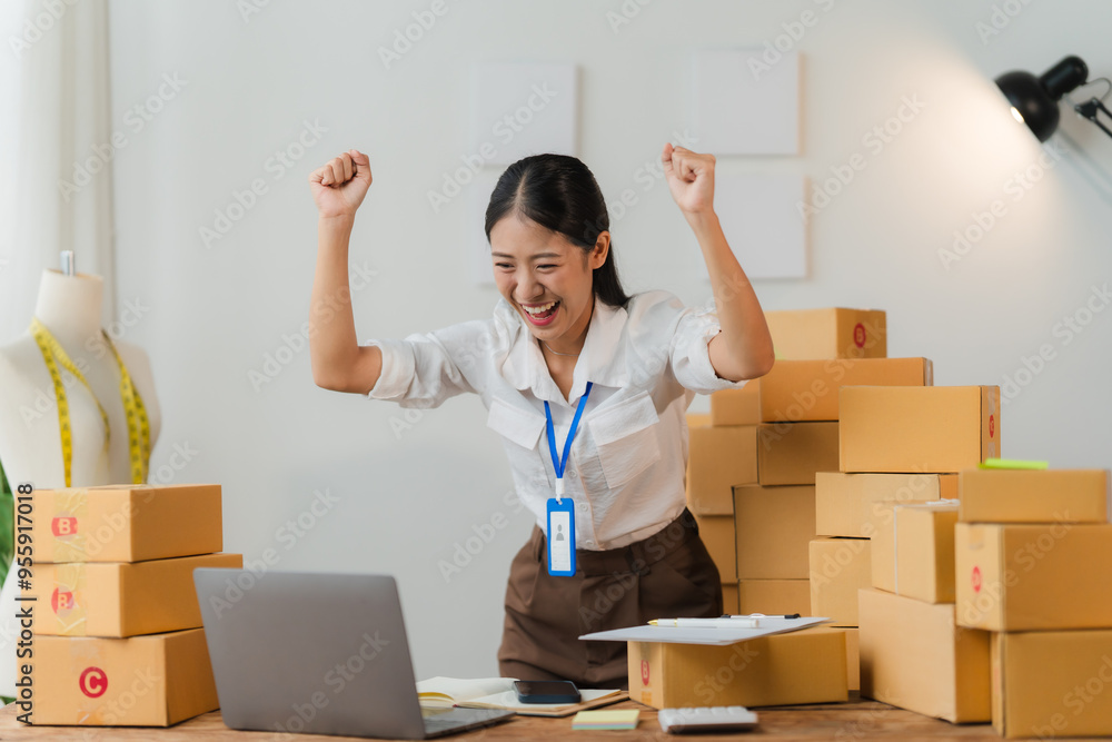 Ecommerce Success - Asian businesswoman celebrating a successful sale in her home office. Ecommerce Success - Asian businesswoman celebrating a successful sale in her home office.
