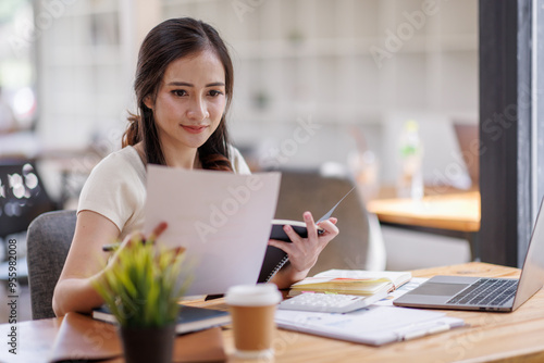 Asian young business woman working on laptop computer reading financial document report in office. Accountant entrepreneur manager businesswoman doing paperwork. Copy space