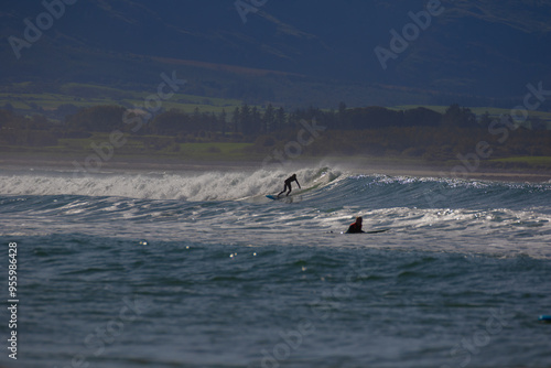 yellowish-white waves with surfers against a blue sky. 