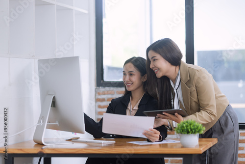 Two Asian young businesswomen working on computer with analyzing financial charts in the modern office, Business financial documents and planning idea project concept.