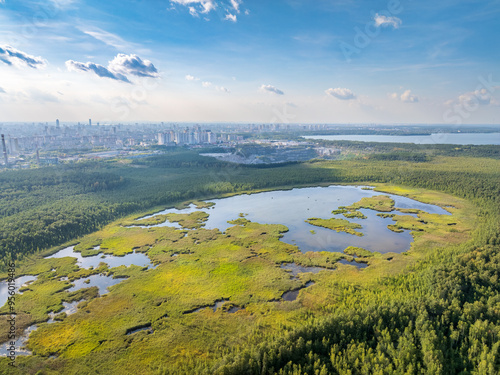 Big lake with green shores in bright sun light and city on horizon, aerial landscape. Recreation concept. Aerial view photo