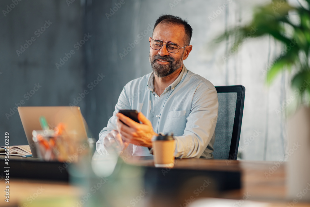 Smiling executive sitting at workspace and contacting clients on a phone Smiling executive sitting at workspace and contacting clients on a phone