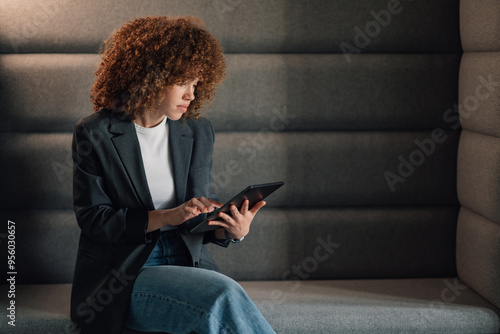 Fashionable businesswoman scrolling on tablet at modern office.