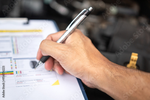 Close-up at a mechanic foreman's hand is checking on multi-point car service guideline checklist form, to verify the car service quality. Expertise working action scene, selective focus. photo
