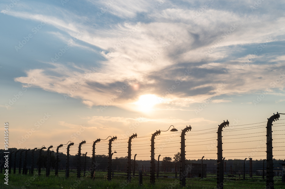 Obraz premium Sunset view of barbed wire fence with dramatic clouds in the sky.