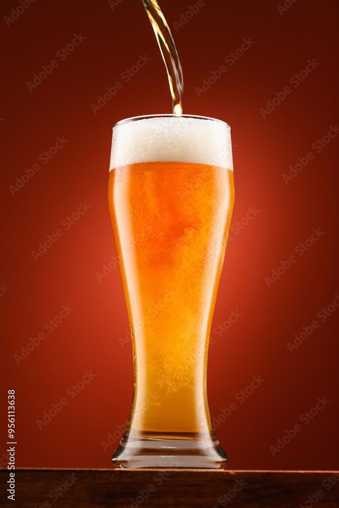 pouring beer into glass, wooden stand, red background, close-up view of object, beer foams and bubbles pouring beer into glass, wooden stand, red background, close-up view of object, beer foams and bubbles