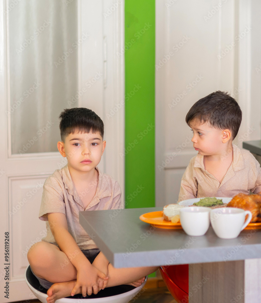 kids siblings eating breakfast in kitchen a sandwich.hungry child boy holding bread with ham in hand. green wall in background, morning time.many products in plate on counter. kids siblings eating breakfast in kitchen a sandwich.hungry child boy holding bread with ham in hand. green wall in background, morning time.many products in plate on counter.