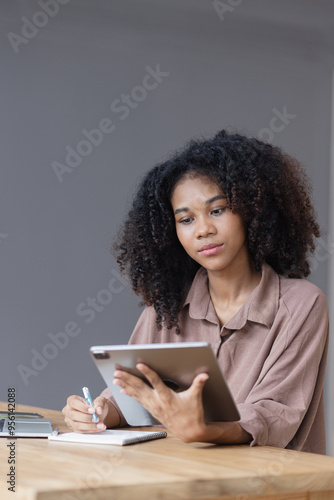 African American businesswoman excited by the good news on the tablet sitting at office desk.