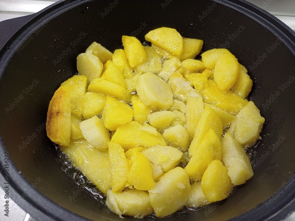 Potato pieces are fried in vegetable oil in a deep frying pan. Potato pieces are fried in vegetable oil in a deep frying pan.