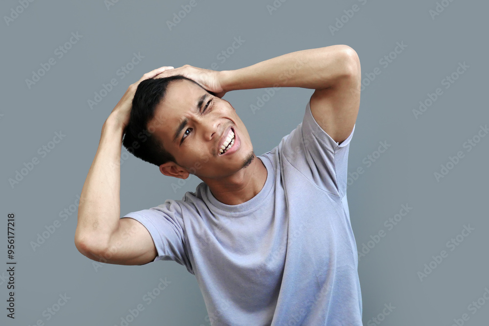 Young Indonesian man holds the side of his head with his hand, his face showing shocked pain after being hit Young Indonesian man holds the side of his head with his hand, his face showing shocked pain after being hit