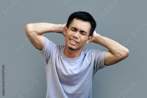 Indonesian male model holds the back of his head with both hands with an expression of pain