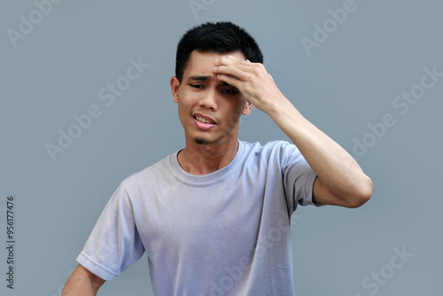 The young Indonesian man pressed his forehead with one hand, his expression showing a severe throb of pain photo