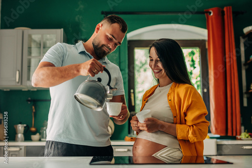 Pregnant woman with husband pouring tea in cup at home