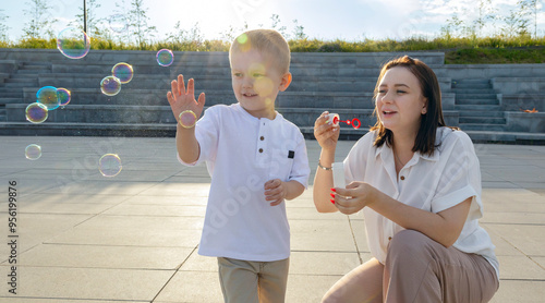 A dark-haired woman blows bubbles with her son.