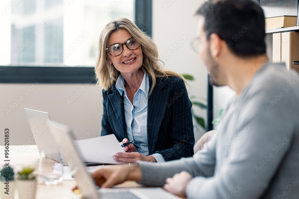 Smiling mature businesswoman talking with coworker at office Smiling mature businesswoman talking with coworker at office
