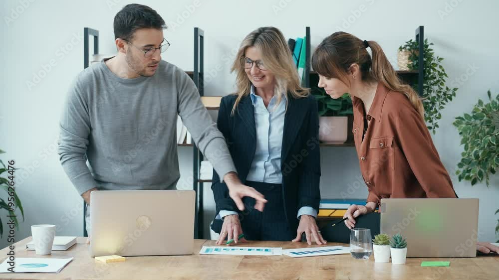 Businessman and woman standing at desk looking at charts Businessman and woman standing at desk looking at charts