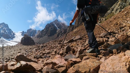 A male traveler is hiking high in the mountains. A man with a backpack and trekking poles hiking alone up a mountain on a sunny day. 2x slow motion photo