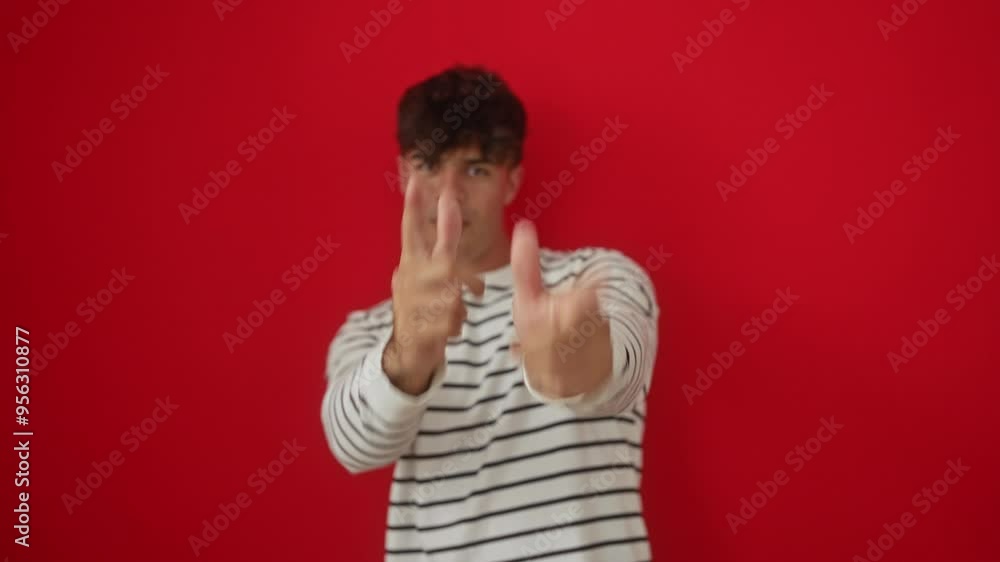 Young hispanic man wearing stripes t shirt standing and pointing fingers to camera with happy and funny expression, radiating good vibes over isolated red background Young hispanic man wearing stripes t shirt standing and pointing fingers to camera with happy and funny expression, radiating good vibes over isolated red background