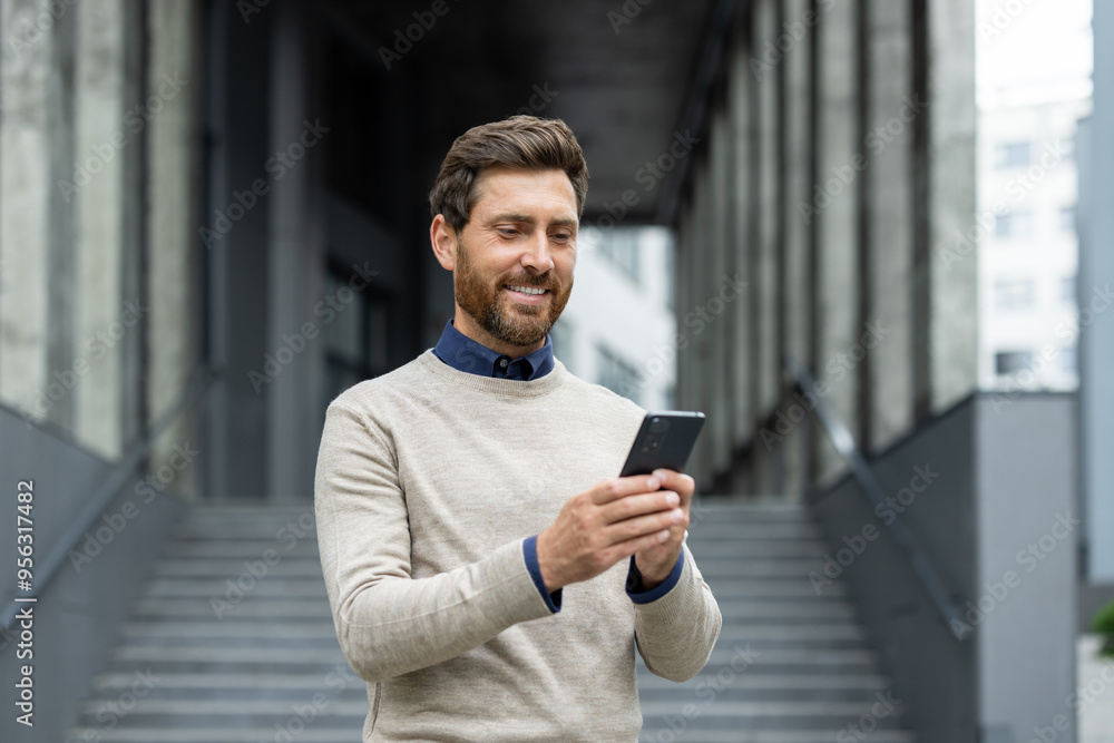 Confident man holding phone, smiling as he stands in front of corporate building. Represents business connectivity, technology, and communication. Ideal image for depicting professional lifestyle Confident man holding phone, smiling as he stands in front of corporate building. Represents business connectivity, technology, and communication. Ideal image for depicting professional lifestyle