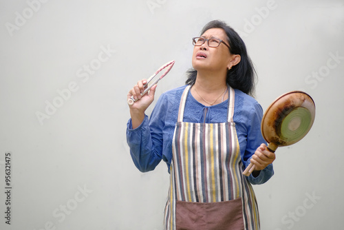 Woman standing and holding kitchen utensils, trying to figure out what to cook for dinner photo