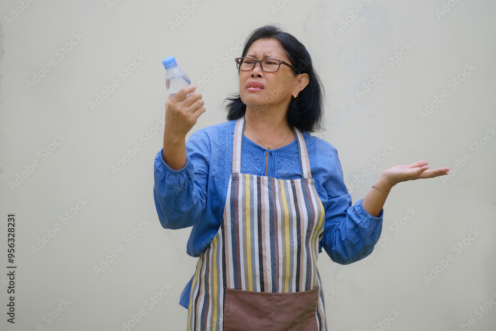 Facial expression of a woman standing and examining the bottled mineral water she is holding in her hand Facial expression of a woman standing and examining the bottled mineral water she is holding in her hand