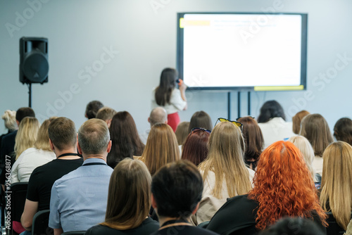 Business seminar featuring a speaker presenting information to a large audience in a conference room setting.