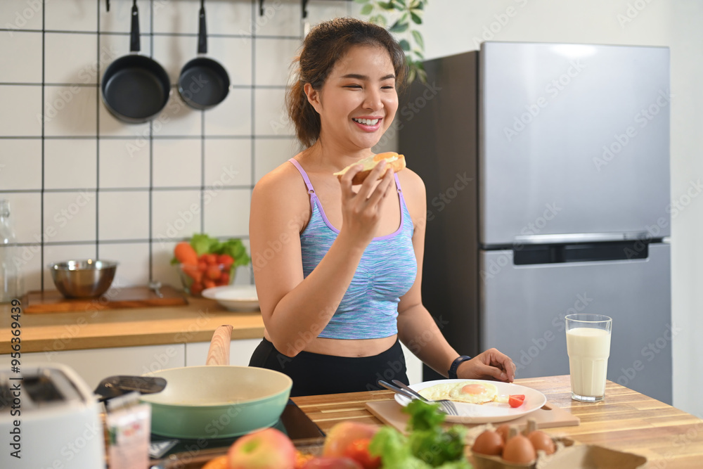 Young woman in sportswear having breakfast with tasty toasted bread and glass of milk in kitchen Young woman in sportswear having breakfast with tasty toasted bread and glass of milk in kitchen