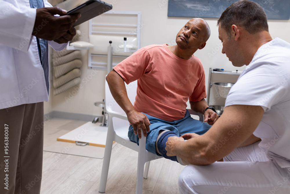 Doctor examining patient's leg while another doctor taking notes in prosthetic lab Doctor examining patient's leg while another doctor taking notes in prosthetic lab
