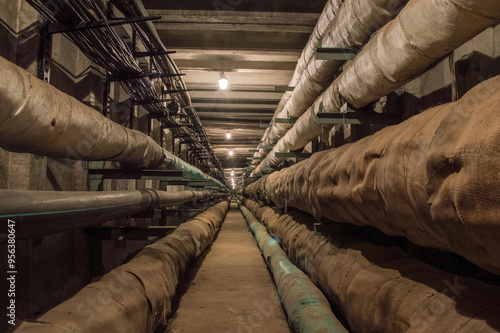 Underground concrete utility tunnel with pipes and wires lit by tungsten bulbs.. This tunnel gives energy, water and heat for industrial and apartment buildings. photo