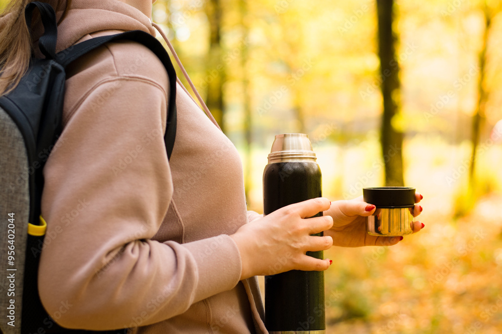 Young girl with backpack on back holding thermos with hot drink, enjoying autumn scenery, copy space, unrecognizable personality. High quality photo Young girl with backpack on back holding thermos with hot drink, enjoying autumn scenery, copy space, unrecognizable personality. High quality photo