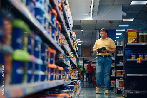 Employee examining products in a retail store aisle while taking notes during the day