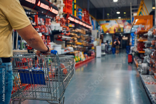 Man pushing a shopping cart through a retail store aisle filled with tools and supplies during daytime hours