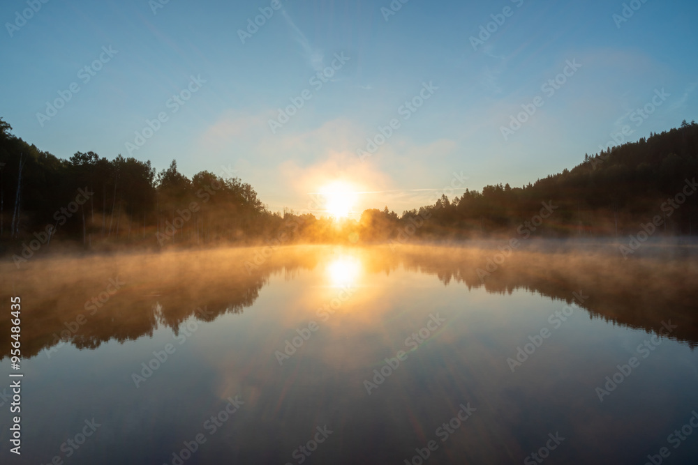 Fototapeta premium Morning sunrise over lake and forest, beautiful blue sky, sun and mist and reflection on the surface of the lake. Summer time.