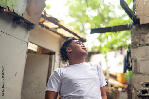 An optimistic man looking up, eyes closed while in front of a slum area. A young Filipino residing in an squatter area visualizing his goals. photo